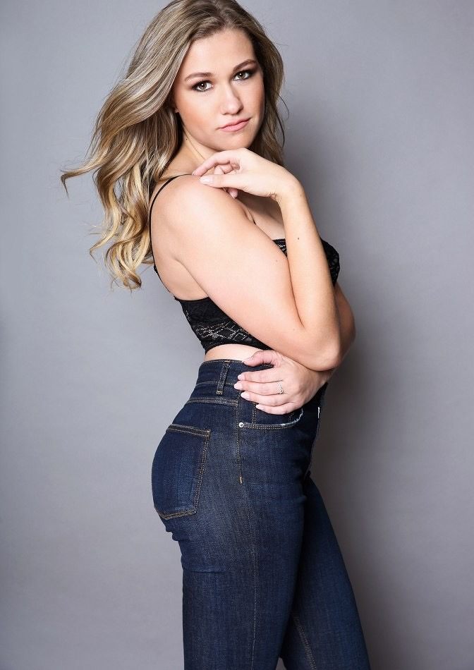 Kari in a black lace top and dark high-waisted jeans, posed against a grey backdrop